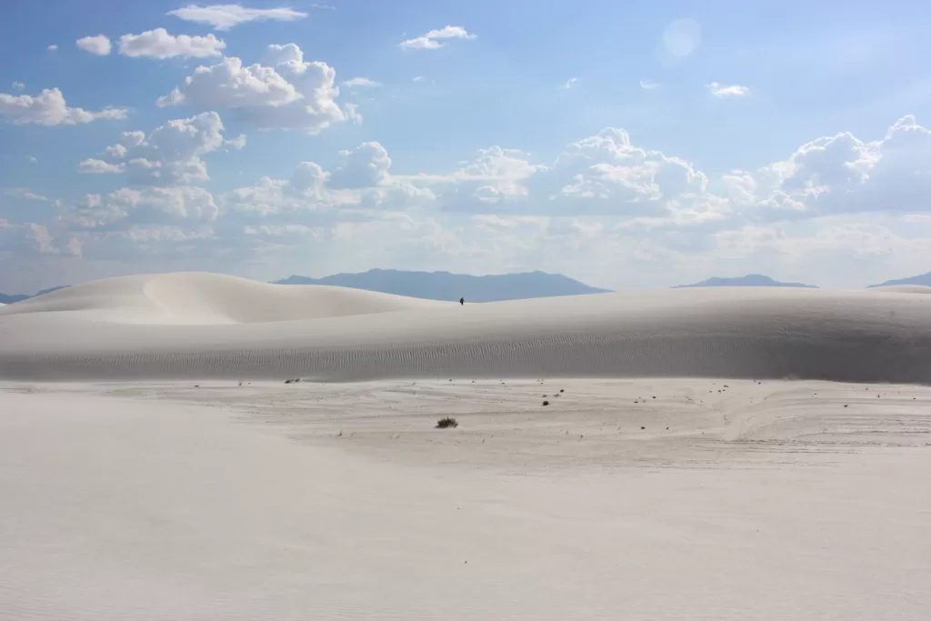 A lone hiker walking among the sand dunes at White Sands National Park.
