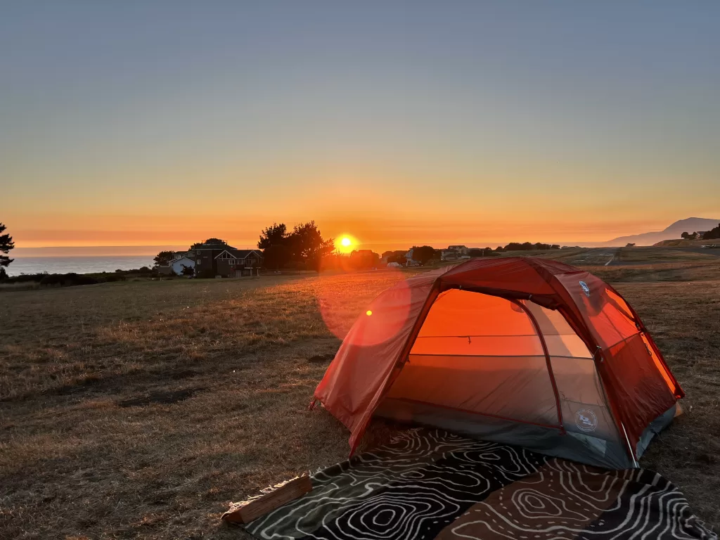 a tent pitched on the grass in Shelter Cove, California with the sun setting over the Pacific Ocean in the background.  