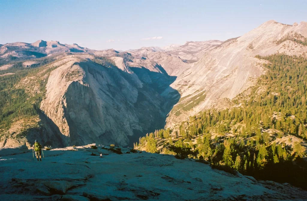 A backpacker hiking down half dome, with the Yosemite high country in the distance.