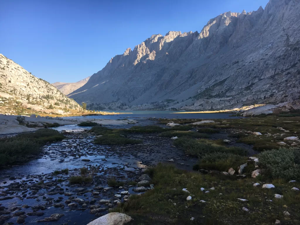 An alpine meadow, flowing river, and towering mountains between Evolution Lake and the Muir Hut on the John Muir Trail.