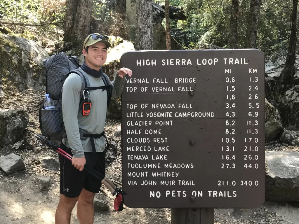 Andrew smiling and standing at the Happy Isles trailhead sign, the northern terminus of the John Muir Trail, just before embarking on his thru-hike. 