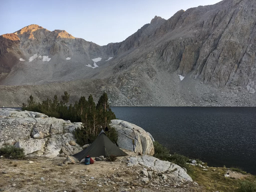 A tent and bear canister next to a lake and large mountain on the John Muir Trail.