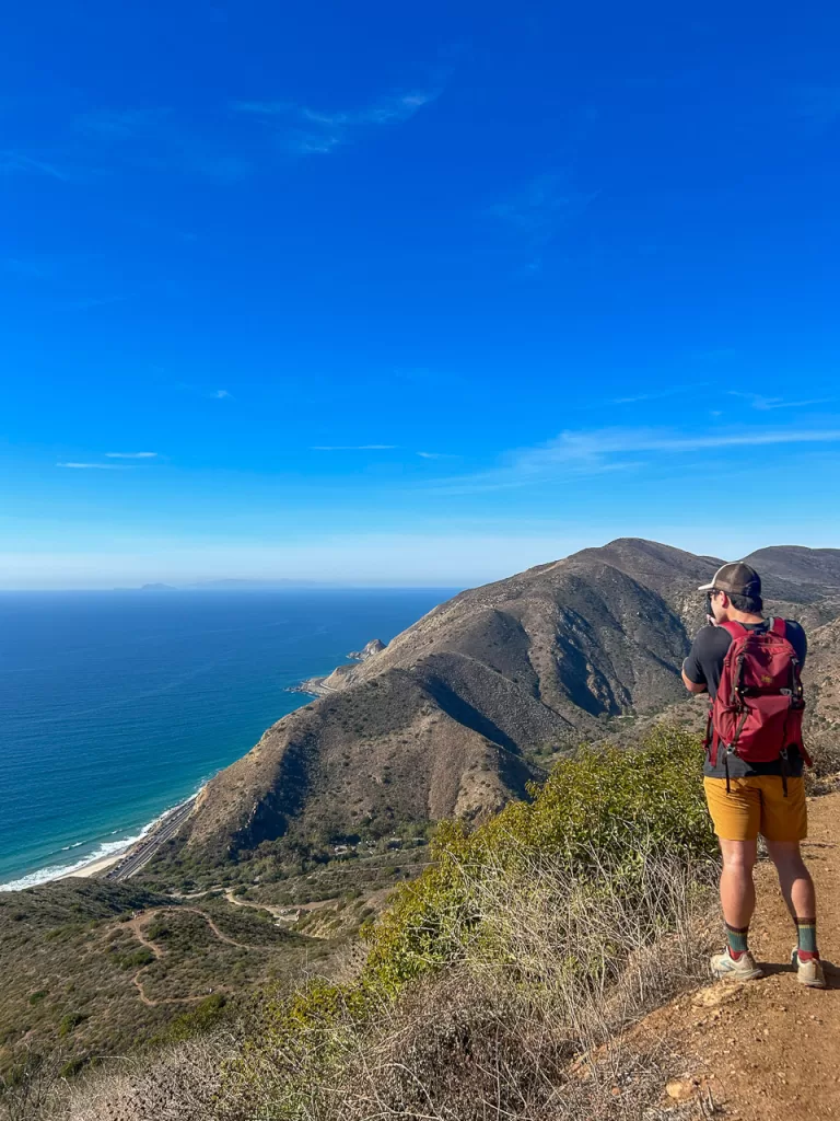 A hiker hiking in the Santa Monica Mountains in Point Mugu State Park taking a photo of the pacific ocean. 