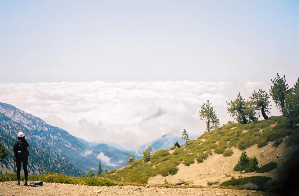 A hiker climbing up the Devil's Backbone Trail to the summit of Mt. Baldy taking in the view above the clouds. 