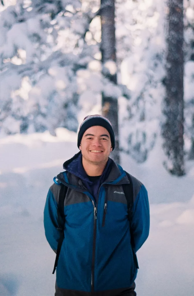 Andrew wearing winter hiking clothes and smiling with snow and trees in the background.