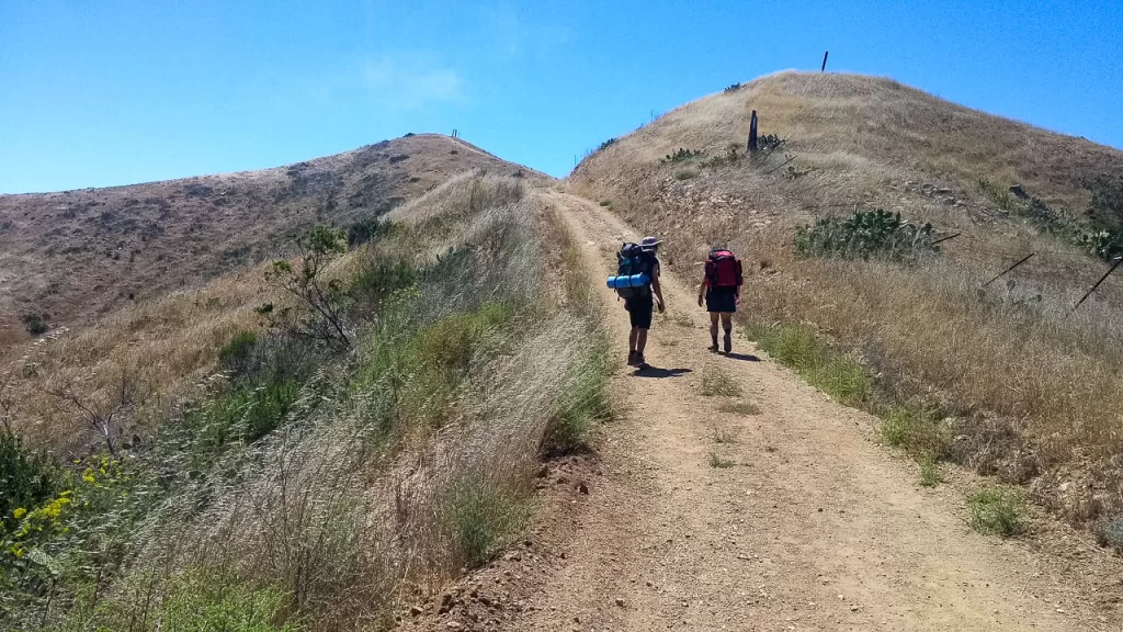 Two hikers climbing up a steep hill on the Trans-Catalina Trail. 