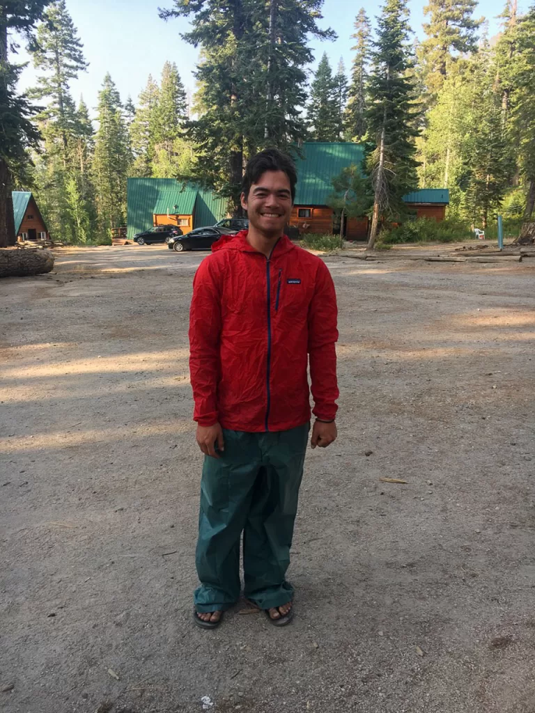 A hiker wearing rain clothes and smiling while his hiking clothes are getting washed. 