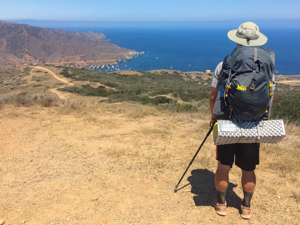 A hiker on the Trans-Catalina Trail staring off into the distance, with Two Harbors and the ocean in the distance.