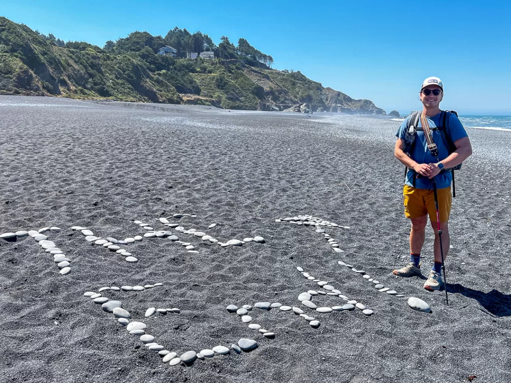 A hiker standing next to a pile of rocks reading "The End" after finishing the Lost Coast Trail.