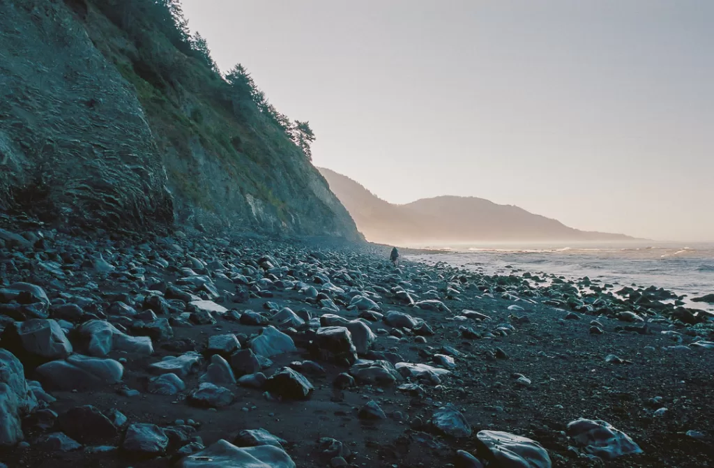 A misty morning on the Lost Coast Trail, with a hiker hiking along the beach. 