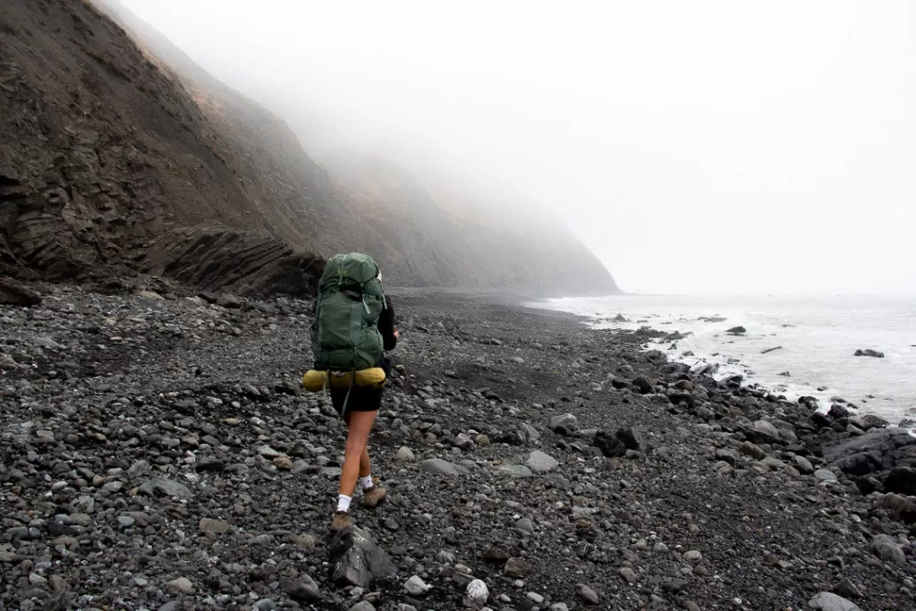 A hiker hiking along the ocean during a foggy day on the Lost Coast Trail. 