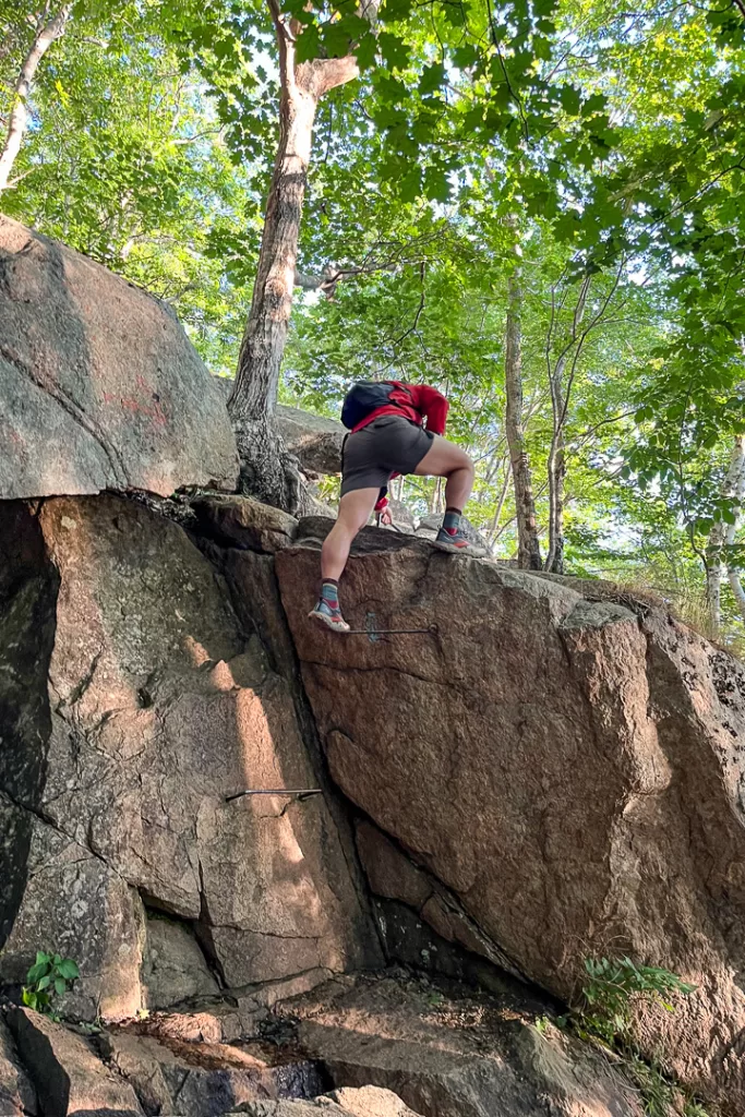 A hiker climbing up iron rungs in Acadia National Park. 