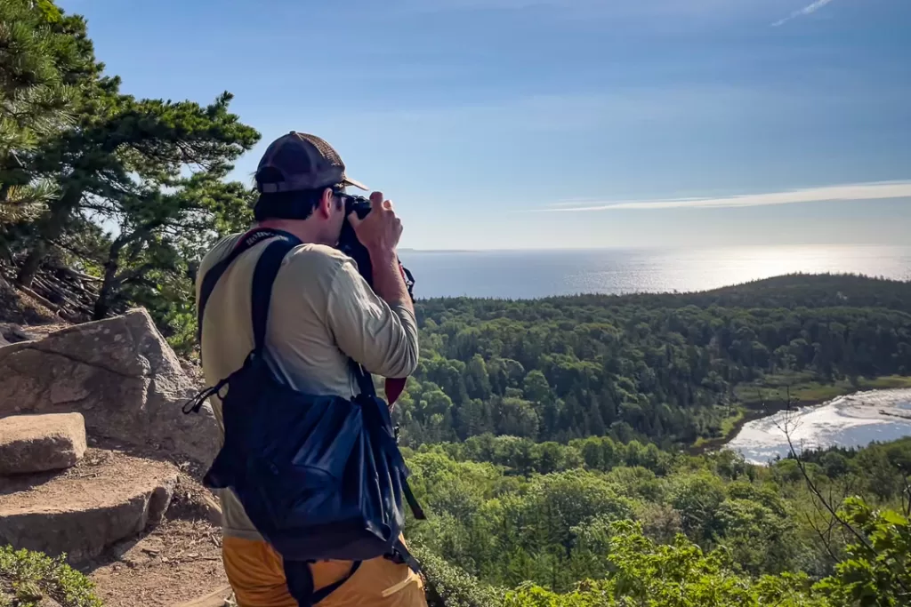 A hiker taking a picture of the scenery in Acadia National Park.