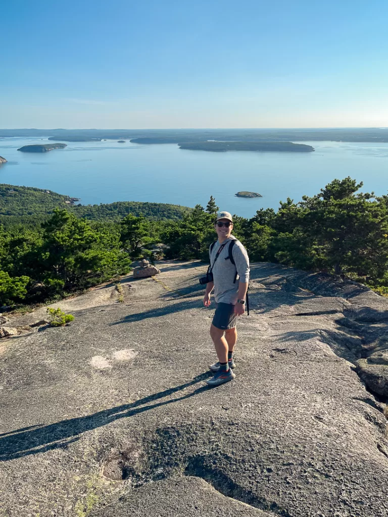 A hiker smiling with the ocean and forests in the background. 