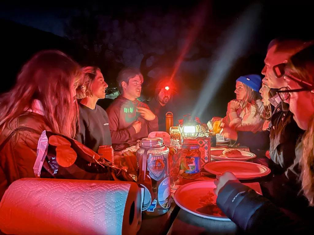 friend chatting and eating on a picnic table at night while camping. 