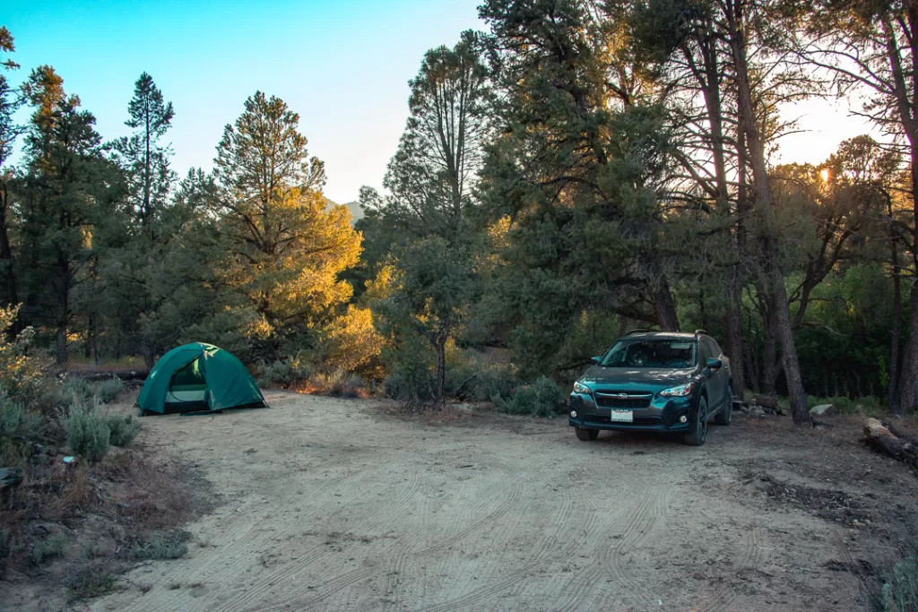 A car and a tent set up in the forest before someone's first time camping. 