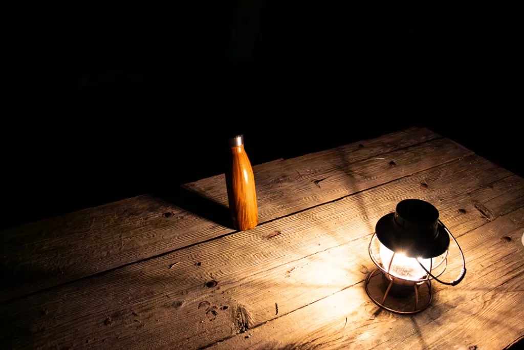 A lantern and water bottle on a picnic table. 