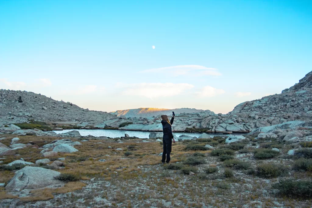 A hiker pointing her phone toward the sky while camping on a mountain.