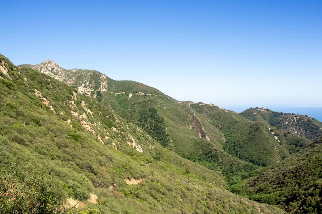 A green mountainside with the ocean in the background.