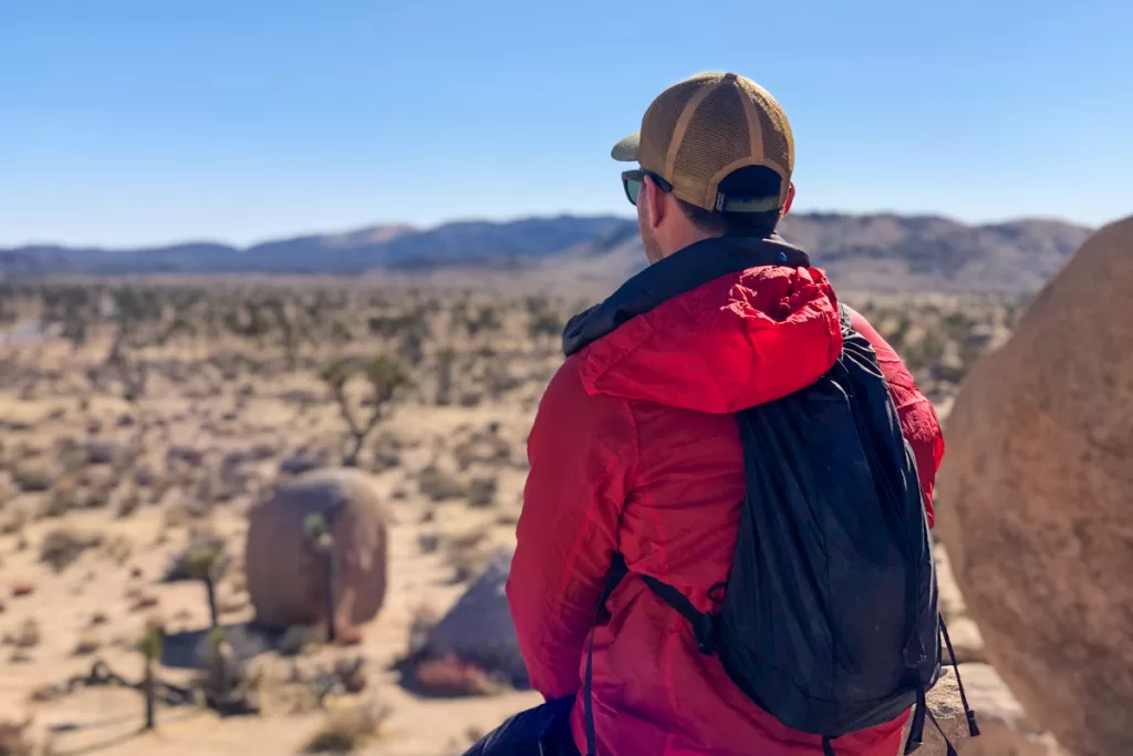 A hiker sitting on a rock looking out at the horizon wearing the REI Co-op Flash 18 backpack.