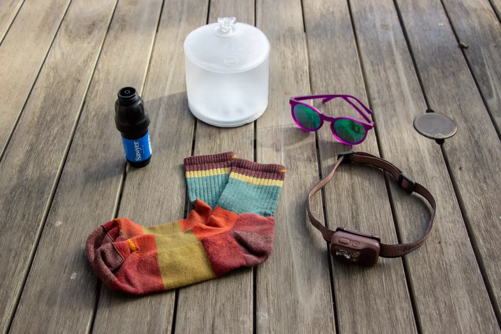 Outdoor gifts under $50 laid out on a table, including a water filter, socks, sun glasses, a headlamp, and a lantern.