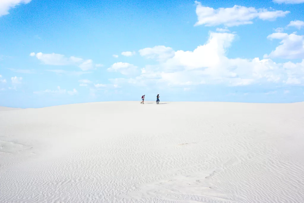 Two hikers walking on white sand dunes. 