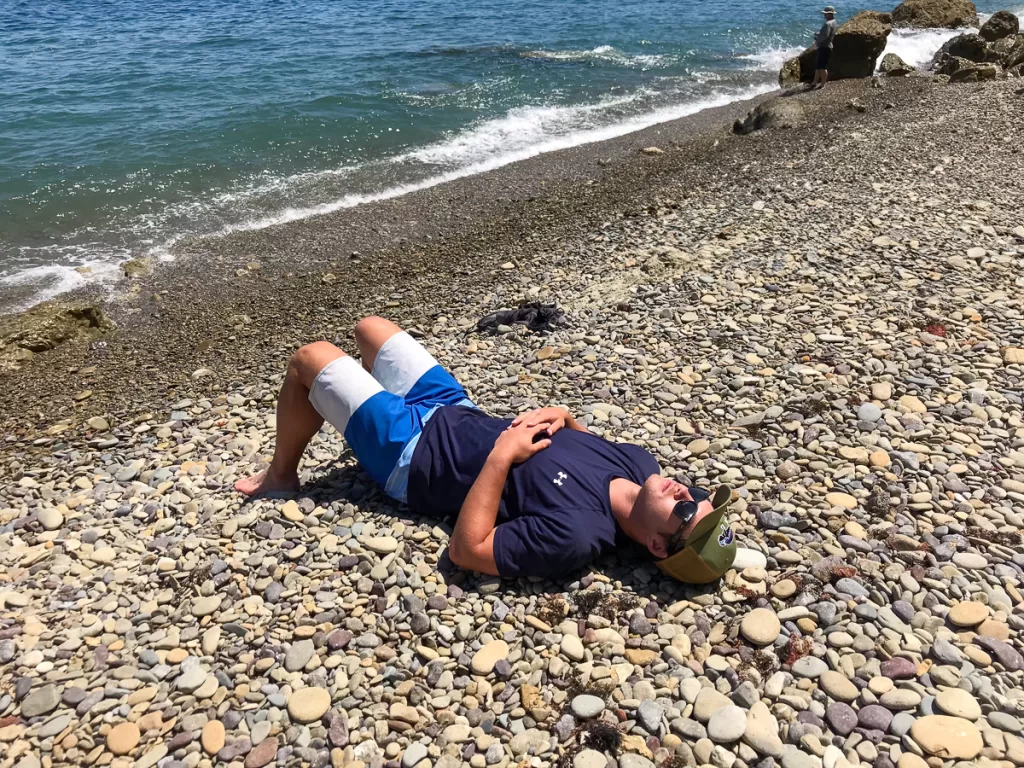 A person asleep on the sand by the beach. 