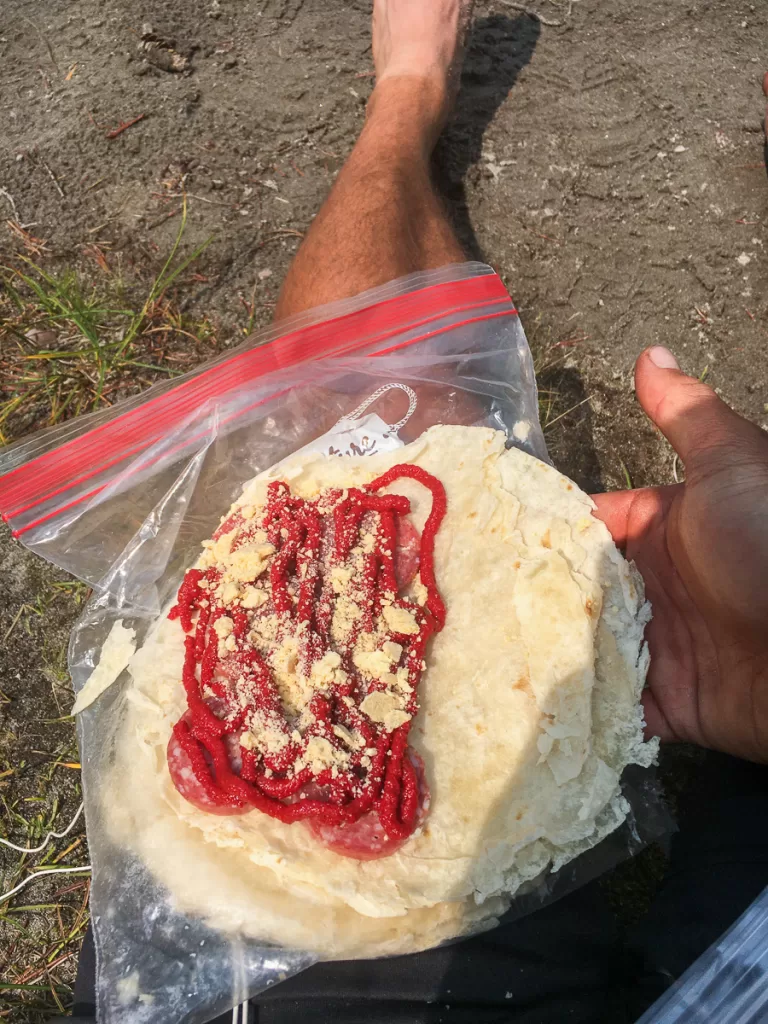 A tortilla with cheese, summer sausage, and tomato paste.