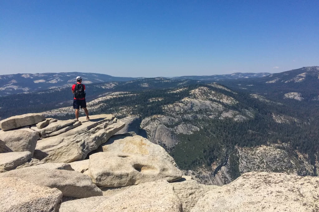 A hiker standing at the top of Half Dome.